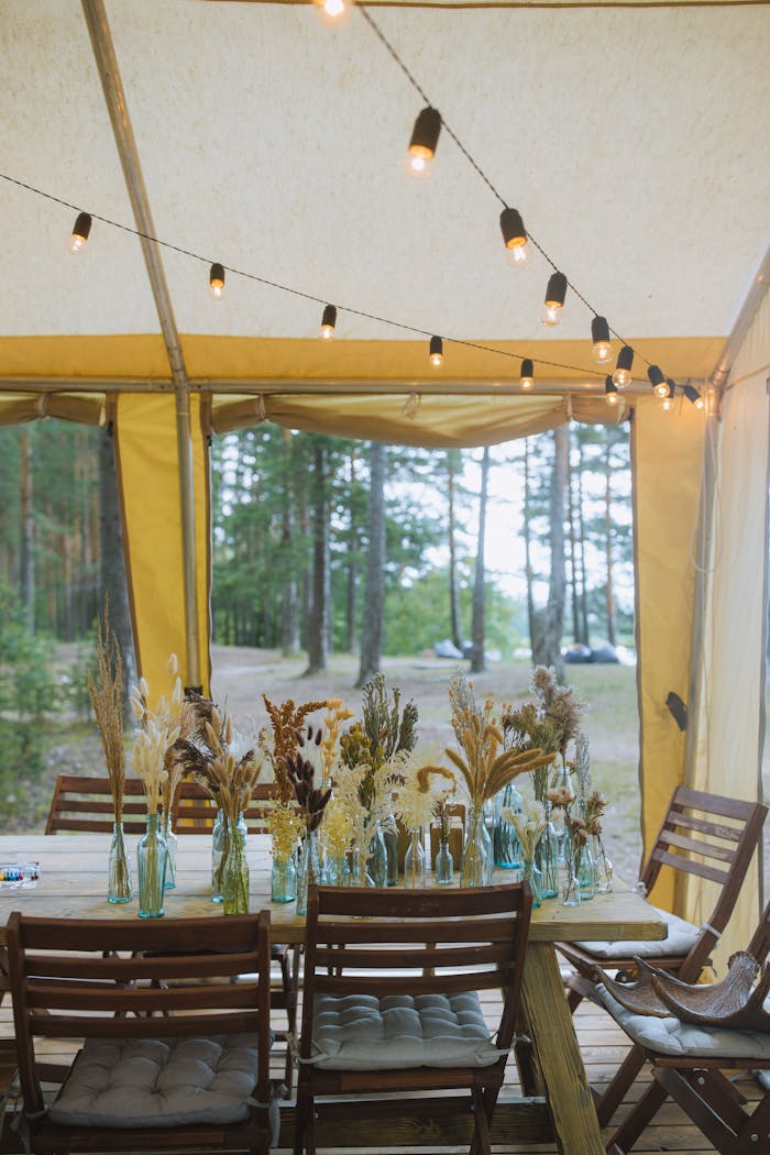 Home Charming outdoor dining setup under a tent with floral centerpieces and string lights, perfect for events.
